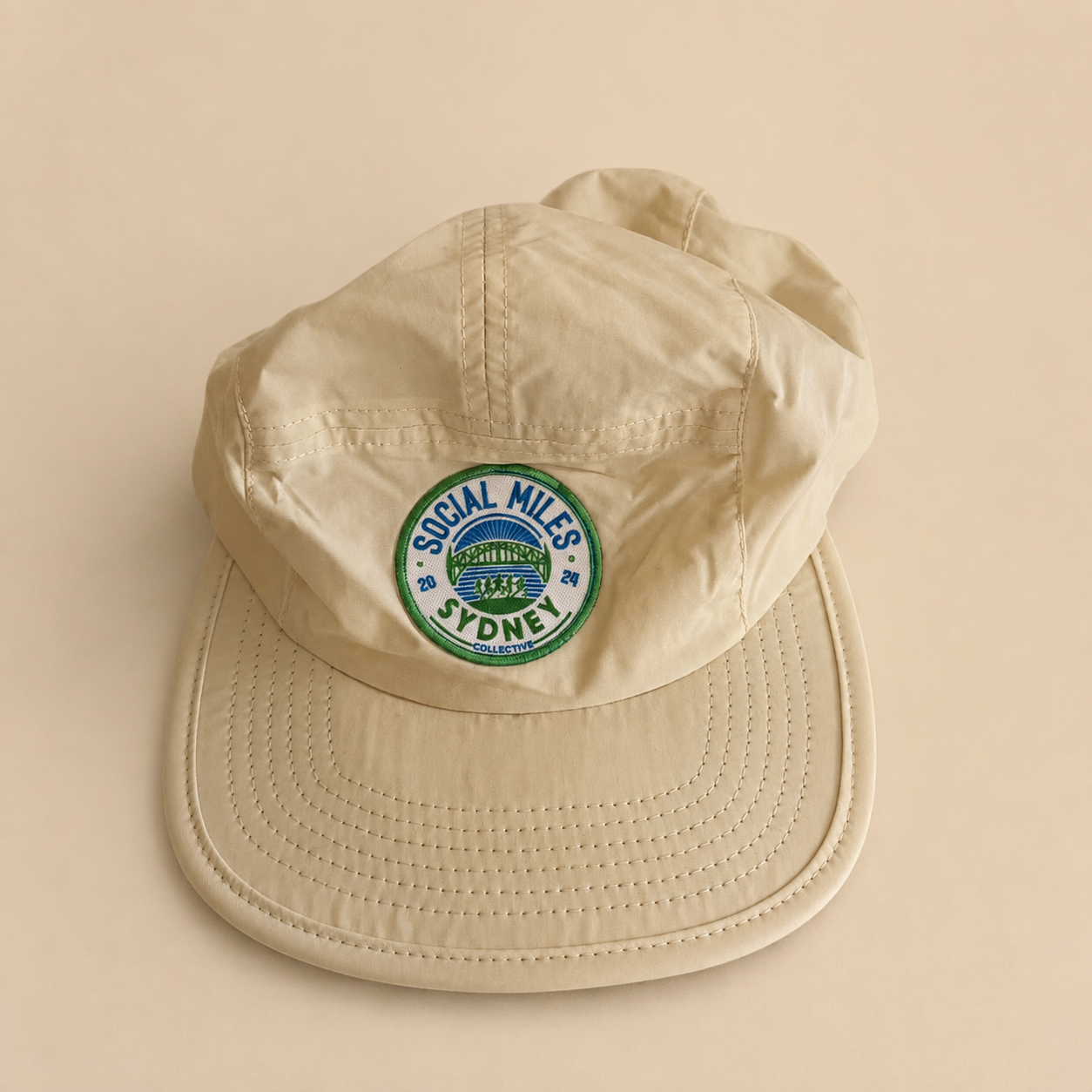 Beige Social Miles Sydney running cap with the embroidered circular club crest.