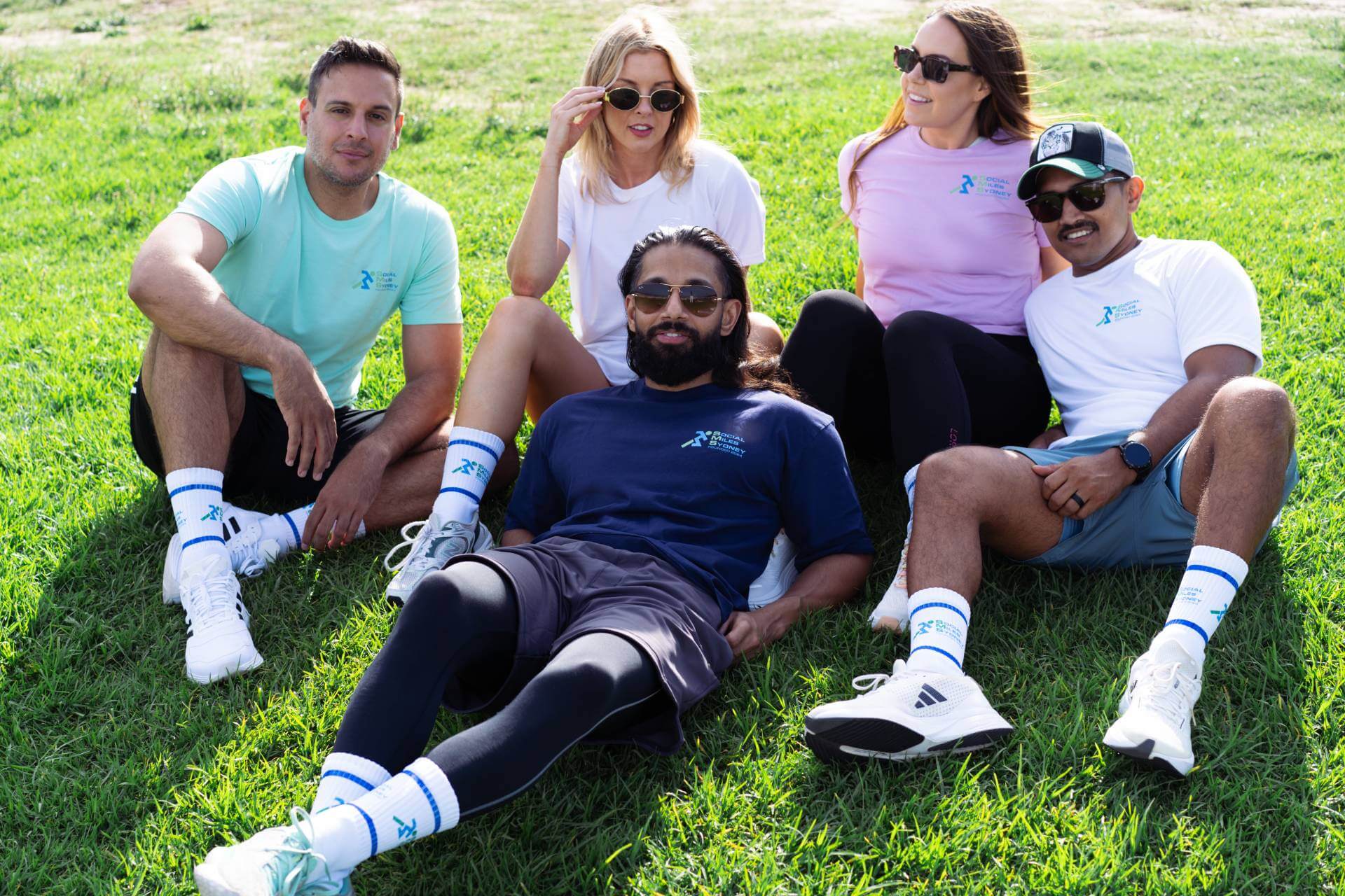 Social Miles Sydney members sitting together on the grass in club shirts and socks after a run and walk.