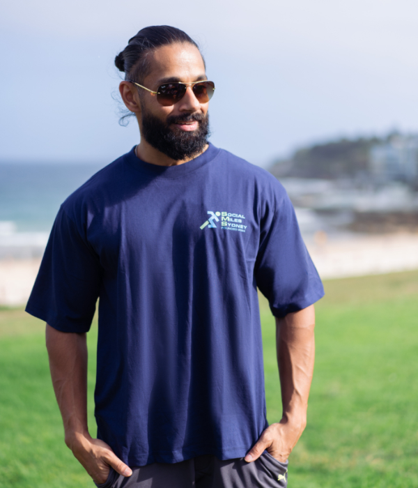 Front view of the navy oversized Social Miles Sydney club tee with a small chest logo, worn on the grass.